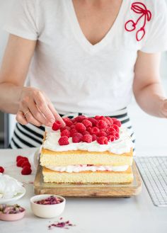 a woman is decorating a cake with raspberries on the top and white frosting