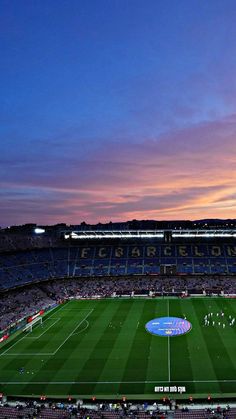 an empty soccer stadium at dusk with the sun setting in the distance and people playing on the field