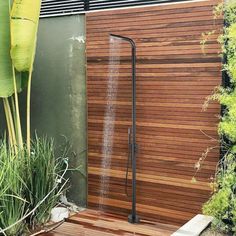 an outdoor shower is shown in front of a wooden wall and planters with green plants