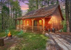 a log cabin in the woods with a fire pit and chairs around it at sunset