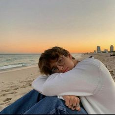 a person sitting on the beach with their arms around each other's shoulders and looking at the camera