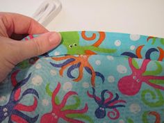 a hand is holding an object in front of a blue and green octopus print fabric