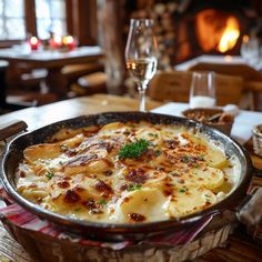 a pan filled with food sitting on top of a table next to a glass of wine