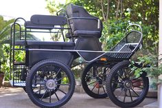 an old fashioned buggy is parked in front of some trees and plants on the sidewalk