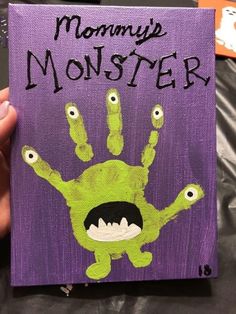 a person holding up a purple book with green monster's handprints on it