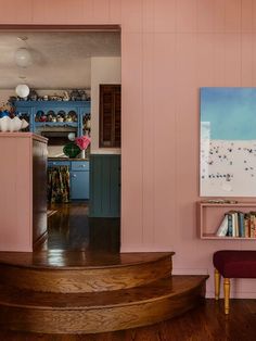 a living room with pink walls and wooden steps leading up to the dining room area