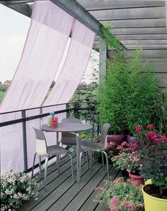 a table and chairs on a wooden deck with flowers in the pots next to it