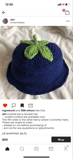 a crocheted blue hat with a green leaf on the front and bottom, sitting on top of a white sheet