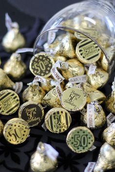 a glass jar filled with gold foiled chocolates on top of a black table