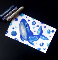 two crayons are sitting next to some watercolors and one has a blue whale on it