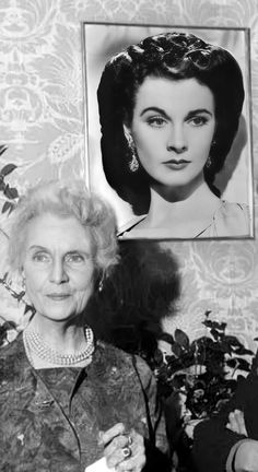 an old black and white photo of a woman in front of a wall with a portrait on it