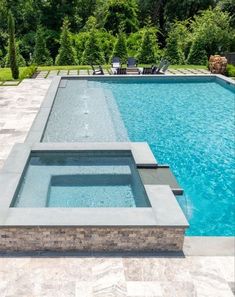 an empty swimming pool surrounded by greenery and stone pavers, with two lounge chairs in the background