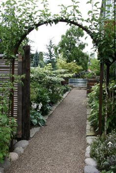 an outdoor garden with lots of plants and gravel path leading to the front door area