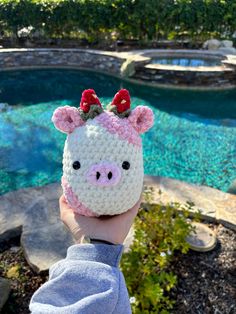 a person is holding up a crocheted pig hat in front of a pool