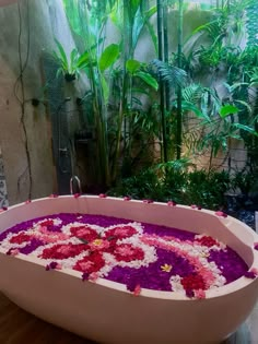 a bathtub filled with lots of flowers on top of a wooden floor next to plants