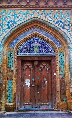 an ornate doorway with two wooden doors and blue tiles on the side of each door