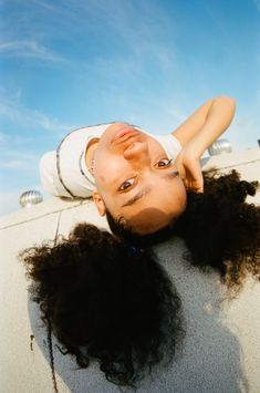 a woman laying on the ground with her hair blowing in the wind and looking at the camera