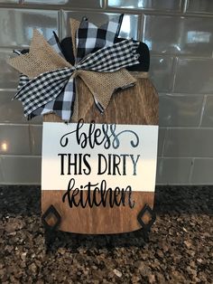 a wooden sign that says, bess this dirty kitchen with black and white gingham