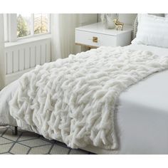 a large white blanket on top of a bed next to a night stand and window