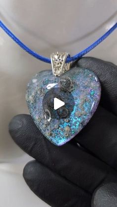 a heart shaped pendant is being held by a person's hand on a blue string