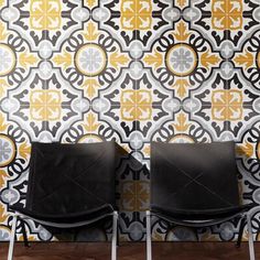 two black chairs sitting next to each other in front of a wall with yellow and white designs on it