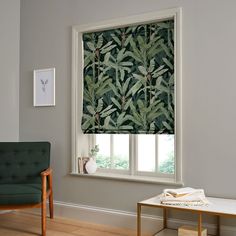 a living room with a chair and window covered in green leafy blind coverings