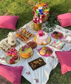 a table topped with cakes and desserts on top of a lush green field covered in pink pillows