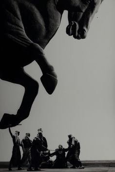 a black and white photo of a horse jumping in the air with people around it