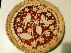 a pie with flowers and leaves on it sitting on top of a white countertop