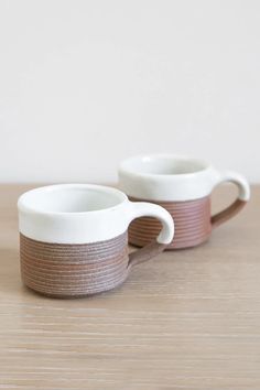 two white and brown cups sitting on top of a wooden table next to each other