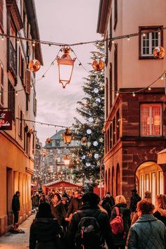 people are walking down an alley way with christmas lights strung over the buildings on both sides