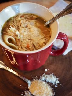 a red cup filled with pasta and parmesan on top of a wooden table