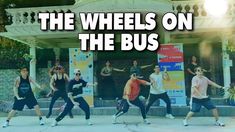 the wheels on the bus are dancing in front of a building with people standing around