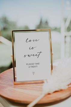 a sign that says love is sweet on top of a wooden table with white feathers