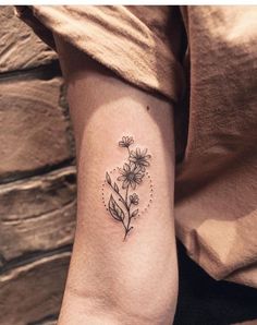 a woman's arm with a small flower tattoo on the left side of her arm