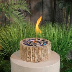 an outdoor fire pit sitting on top of a cement block in front of tall grass