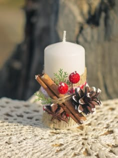 a white candle sitting on top of a table next to pine cones and cinnamon sticks