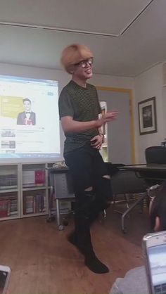 a man standing in front of a projector screen holding a cup and wearing glasses