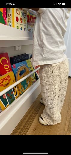 a toddler standing in front of a bookshelf on the floor next to a book shelf