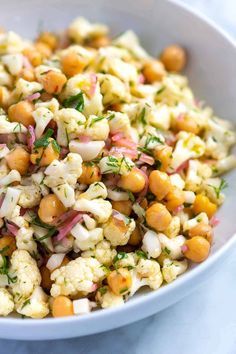 a white bowl filled with chickpeas and garbanzo sprinkled with herbs