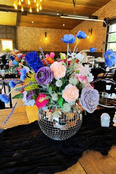 a disco ball vase filled with colorful flowers on top of a wooden table covered in black cloth