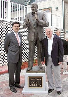 two men standing next to a statue of a man with a microphone in his hand