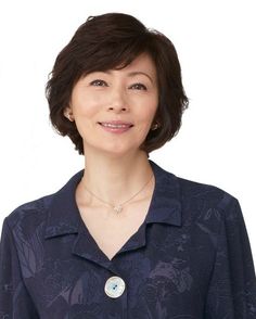 a woman with short hair wearing a blue shirt and smiling at the camera while standing in front of a white background