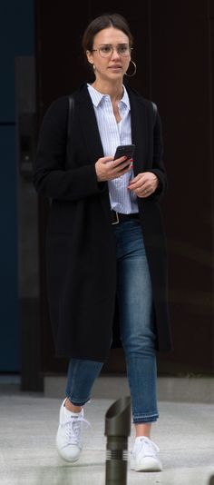 a woman walking down the street while looking at her cell phone and wearing white sneakers