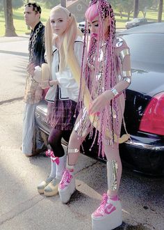 two women dressed in pink and silver are standing next to a car with chains on it