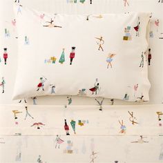 a bed with white sheets and colorful illustrations on the pillowcase, along with two matching pillows