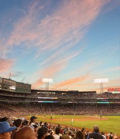 a baseball stadium filled with lots of people sitting in the bleachers at sunset