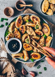 someone holding chopsticks over a plate of dumplings with sauce on the side