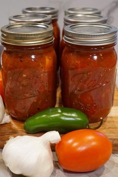 several jars filled with different types of food sitting on a cutting board next to garlic and tomatoes