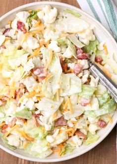 a white bowl filled with salad on top of a wooden table next to a fork